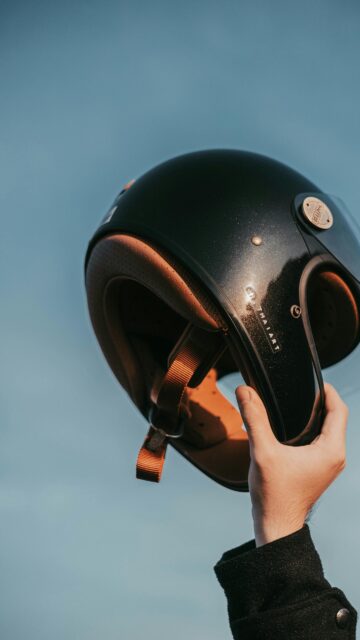 Black Vintage Motorcycle Helmet Held Against Blue Sky Wallpaper