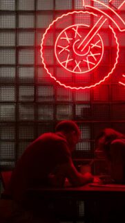 Couple Sitting Under Red Neon Motorcycle Light Phone Wallpaper