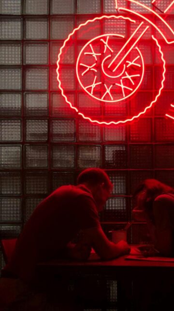 Couple Sitting Under Red Neon Motorcycle Light Phone Wallpaper