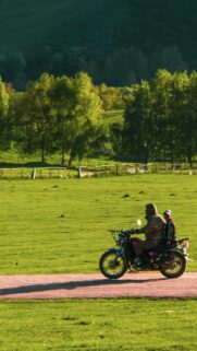 Rider and Child on Motorcycle in Green Nature Field Mobile Wallpaper