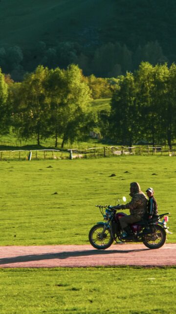 Rider and Child on Motorcycle in Green Nature Field Mobile Wallpaper