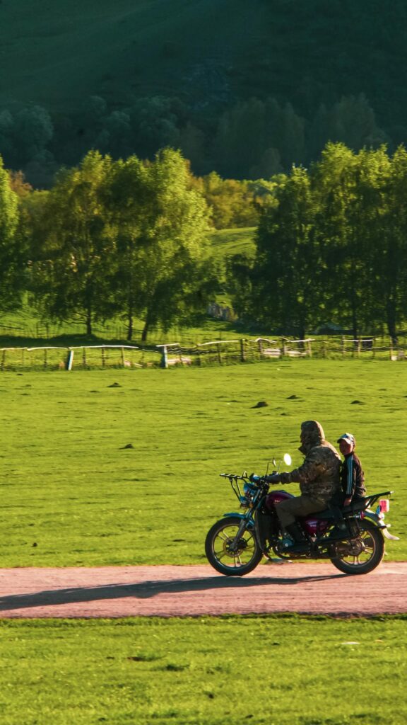 Rider and Child on Motorcycle in Green Nature Field Mobile Wallpaper