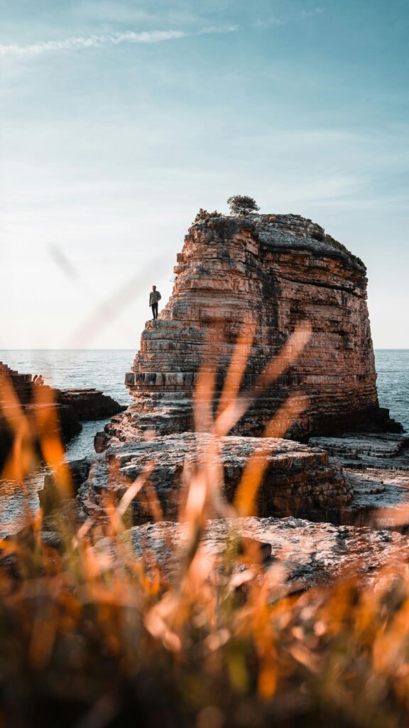 Stunning Man Standing on a Massive Coastal Rock Formation Phone Wallpaper