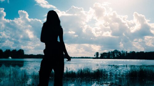 Silhouette of Woman Standing by Serene Lake Under Cloudy Sky 4K Wallpaper
