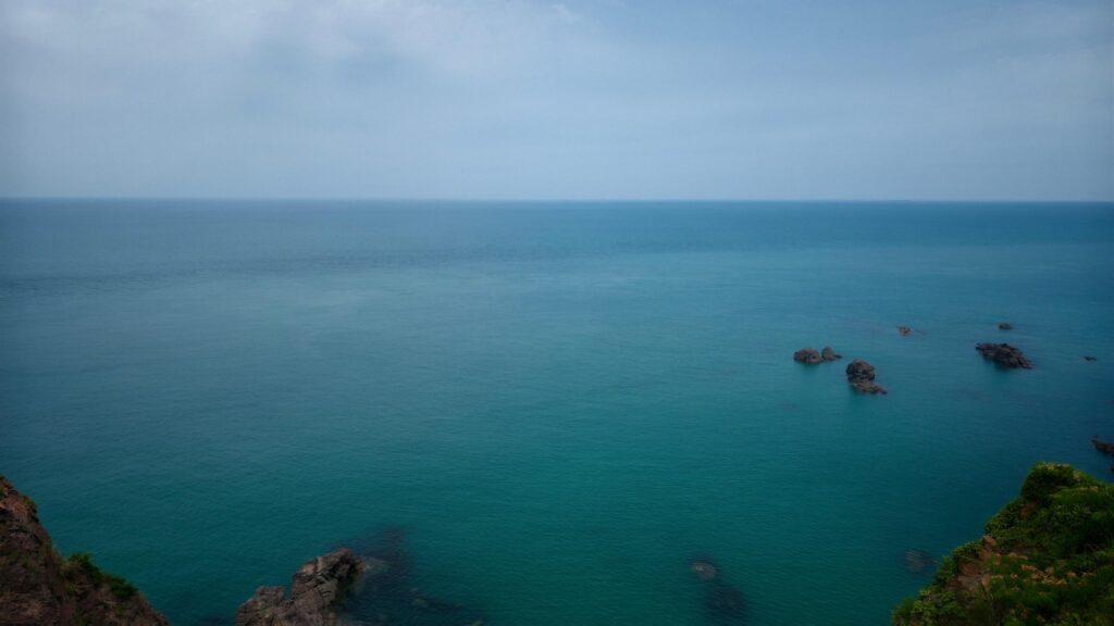 Serene Blue Ocean Horizon with Coastal Rocks Desktop Wallpaper