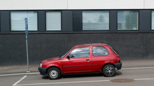 Red Nissan Micra Parked Against Modern Building Desktop Wallpaper