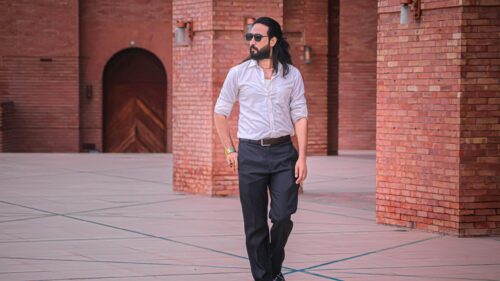 Stylish Man with Long Hair Walking in Architectural Brick Courtyard 4K Wallpaper
