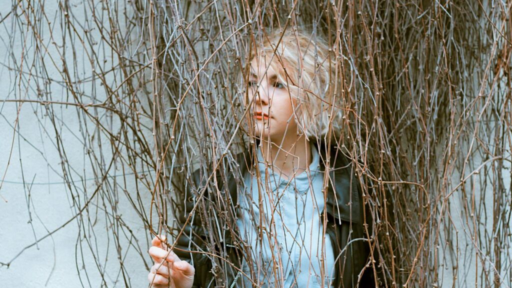 Blonde Girl Peering Through Bare Tree Branches 4K Desktop Wallpaper
