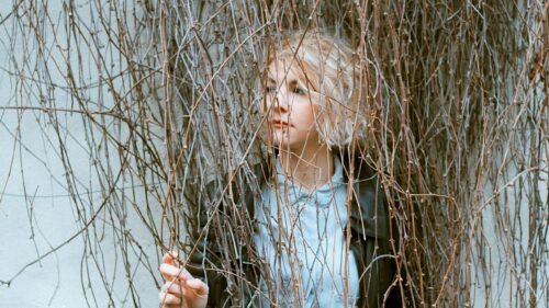 Blonde Girl Peering Through Bare Tree Branches 4K Desktop Wallpaper