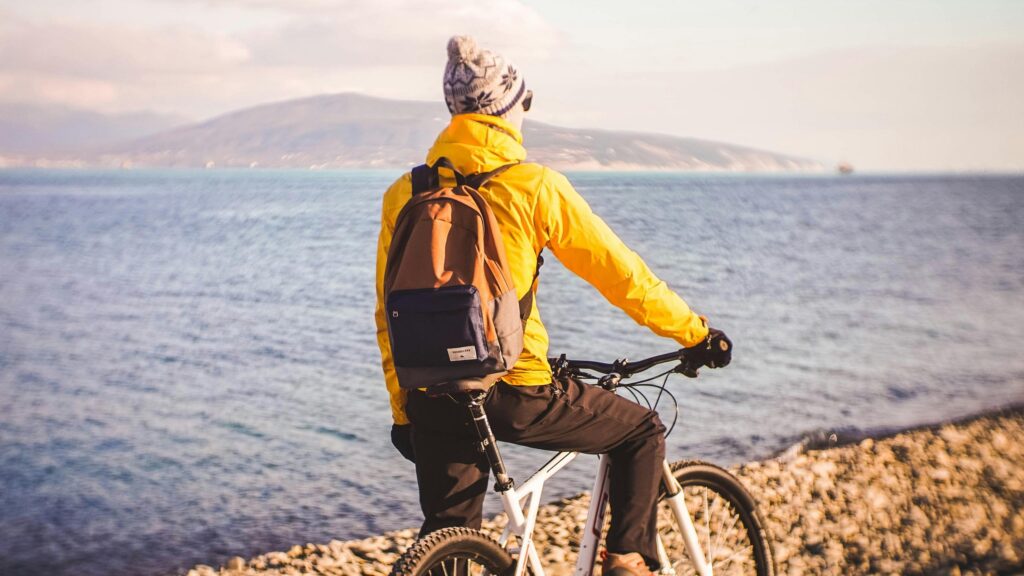 Cyclist on Sunny Pebble Beach with Sea View 4K Desktop Wallpaper