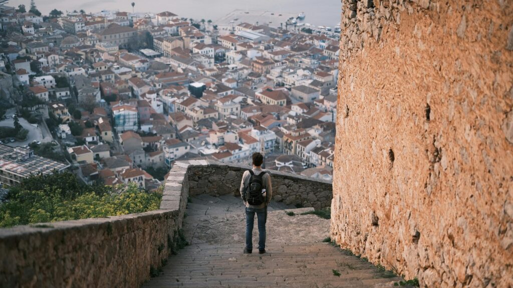 Man Standing on Ancient Stairs Overlooking Coastal Greek Town 4K Wallpaper