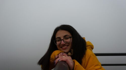 Smiling Girl in Yellow Jacket Leaning on Railing Desktop Wallpaper