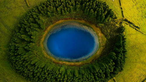 Stunning Aerial View of a Circular Blue Crater Lake Surrounded by Lush Green Forest 4K Wallpaper
