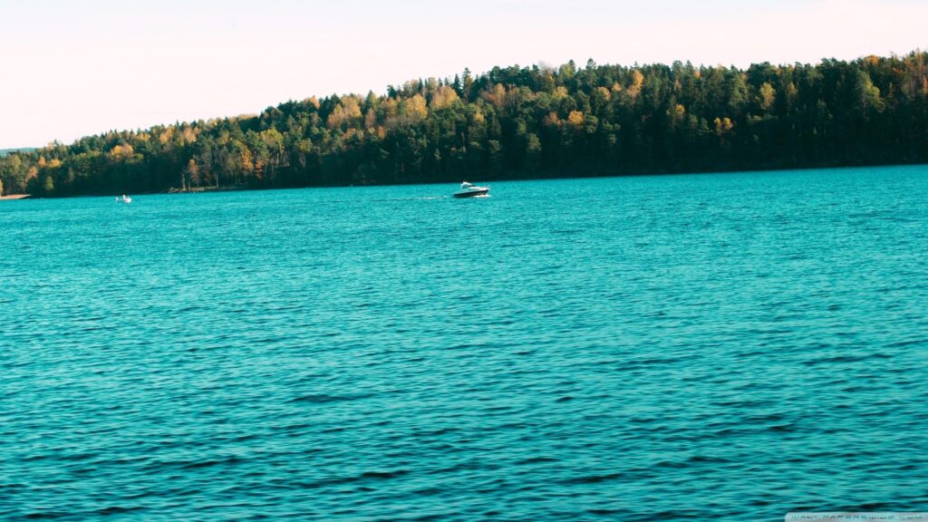 Boats Cruising on a Serene Blue Lake with Autumn Forest Backdrop 4K Wallpaper