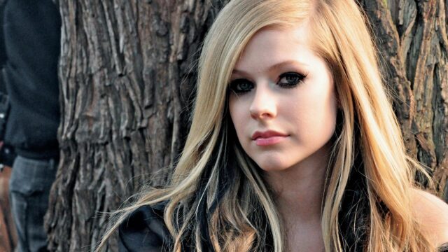 Stunning Portrait of Avril Lavigne with Blonde Hair Against a Rustic Tree Backdrop 4K Wallpaper