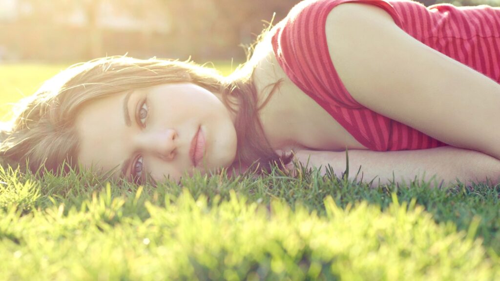 Beautiful Young Woman Resting on Lush Green Grass at Sunset 4K Desktop Wallpaper