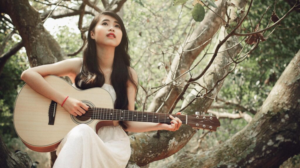 Dreamy Young Woman Playing Acoustic Guitar in Forest Setting Desktop Wallpaper