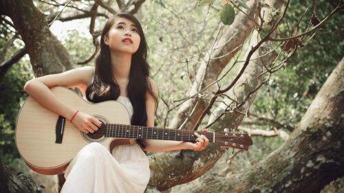 Dreamy Young Woman Playing Acoustic Guitar in Forest Setting Desktop Wallpaper