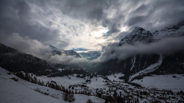 Stunning Snowy Mountain Village Under Dramatic Cloudy Sky 4K Wallpaper