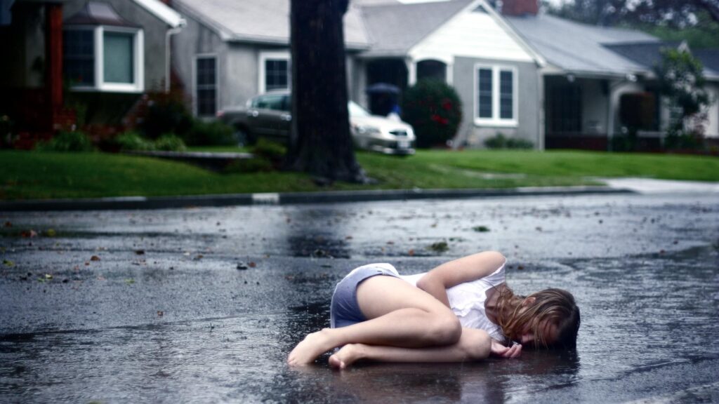 Sad Young Woman Lying Alone on Wet Asphalt Road in Rain 4K Desktop Wallpaper