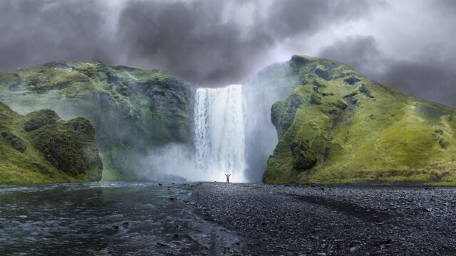 Majestic Skogafoss Waterfall Iceland Person Standing Under Stormy Sky 4K Desktop Wallpaper