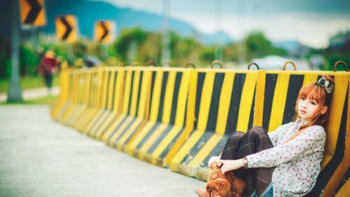 Beautiful Young Woman Sitting Against Yellow Road Barriers Desktop Wallpaper