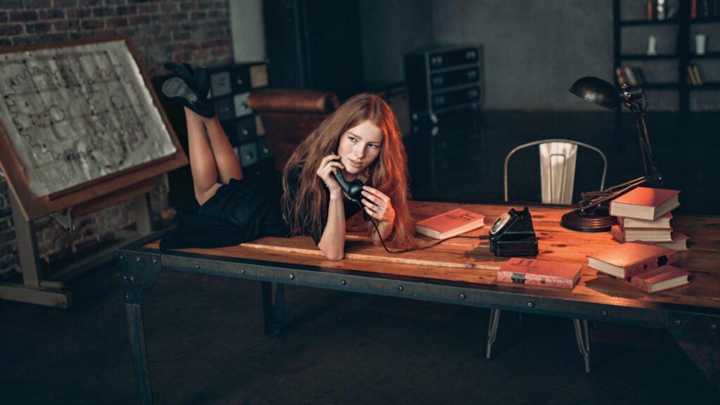 Redheaded Woman Sitting on Desk with Vintage Telephone Desktop Wallpaper
