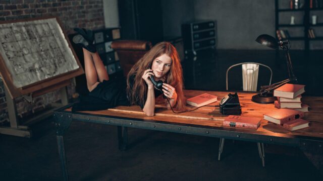 Redheaded Woman Sitting on Desk with Vintage Telephone Desktop Wallpaper