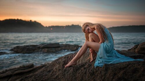 Beautiful Blonde Woman Sitting on Coastal Rocks at Sunset Desktop Wallpaper