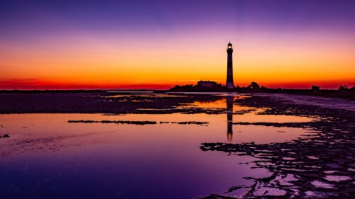 Stunning Lighthouse Silhouette at Sunset Over Calm Coastal Waters 4K Desktop Wallpaper