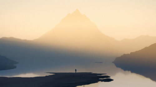 Solitary Traveler Standing Before a Majestic Misty Mountain Lake Desktop Wallpaper