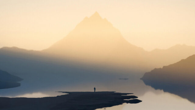 Solitary Traveler Standing Before a Majestic Misty Mountain Lake Desktop Wallpaper