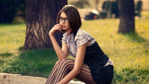 Stylish Young Woman Wearing Glasses in a Park Setting Desktop Wallpaper