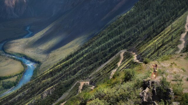 Woman Standing on a Rocky Cliff Above a Winding Mountain Road Desktop Wallpaper