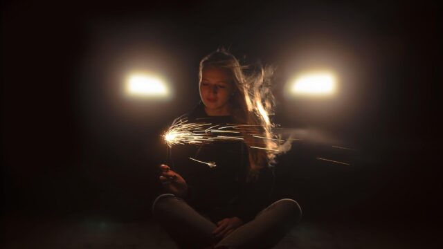 Girl Holding a Sparkling Sparkler in Front of Car Headlights PC Wallpaper