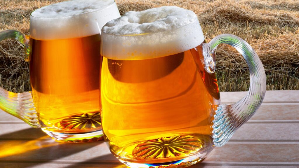 Two Cold Glasses of Golden Beer with Frothy Foam on Hay Background Desktop Wallpaper