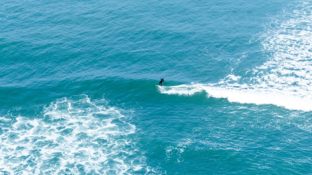 Lone Surfer Riding a Turquoise Ocean Wave 4K Wallpaper