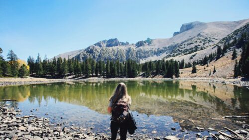 Woman Hiker Standing by Alpine Lake Beneath Mountain Peak Desktop Wallpaper