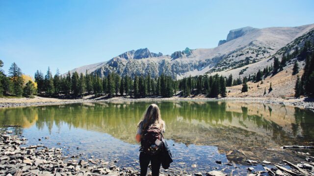 Woman Hiker Standing by Alpine Lake Beneath Mountain Peak Desktop Wallpaper