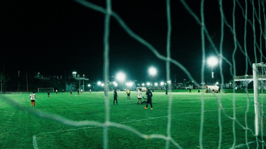 Night Soccer Match Seen Through Goal Net 4K Wallpaper