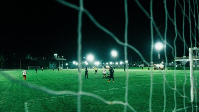 Night Soccer Match Seen Through Goal Net 4K Wallpaper