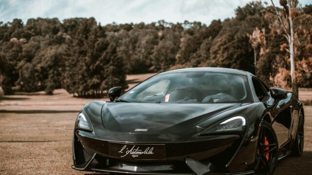 Sleek Black McLaren Sports Car Parked on Countryside Grass 4K Wallpaper