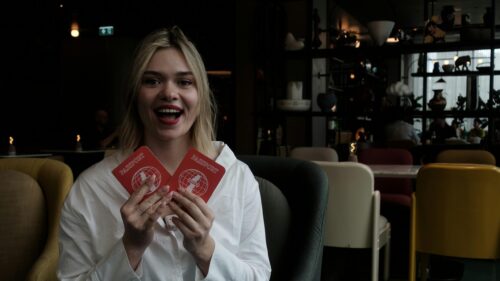 Excited Woman Holding Two Passports in Modern Lounge 4K Wallpaper