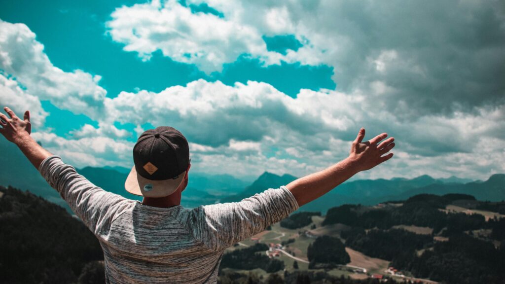 Man Celebrating on Mountain Top Overlooking Valley 4K Desktop Wallpaper