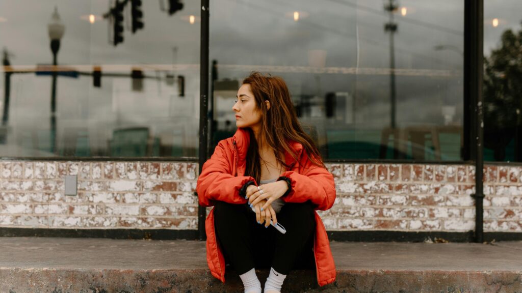 Woman Sitting Outside in Red Jacket Moody Street Photography 4K Wallpaper