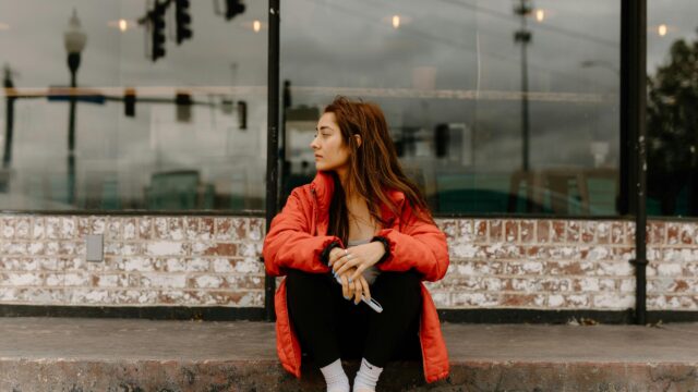 Woman Sitting Outside in Red Jacket Moody Street Photography 4K Wallpaper