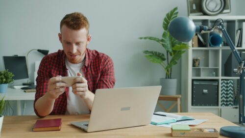 Young Man Playing Mobile Game at Modern Home Office Desk 4K Wallpaper