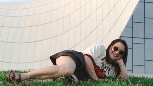 Asian Girl Relaxing on Grass by Modern Architecture 4K Wallpaper