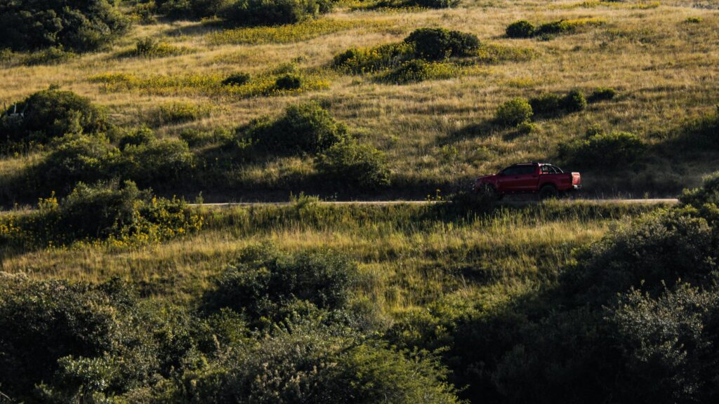 Red Pickup Truck Driving Through Grassy Hills Desktop Wallpaper