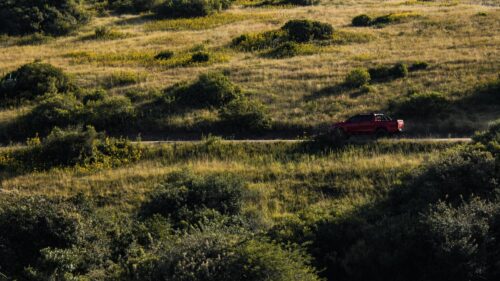 Red Pickup Truck Driving Through Grassy Hills Desktop Wallpaper